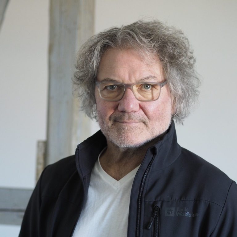 Inhaber Elmar Dräger mit grauen Locken und Brille, trägt ein schwarzes Jacket und ein weißes T-Shirt.