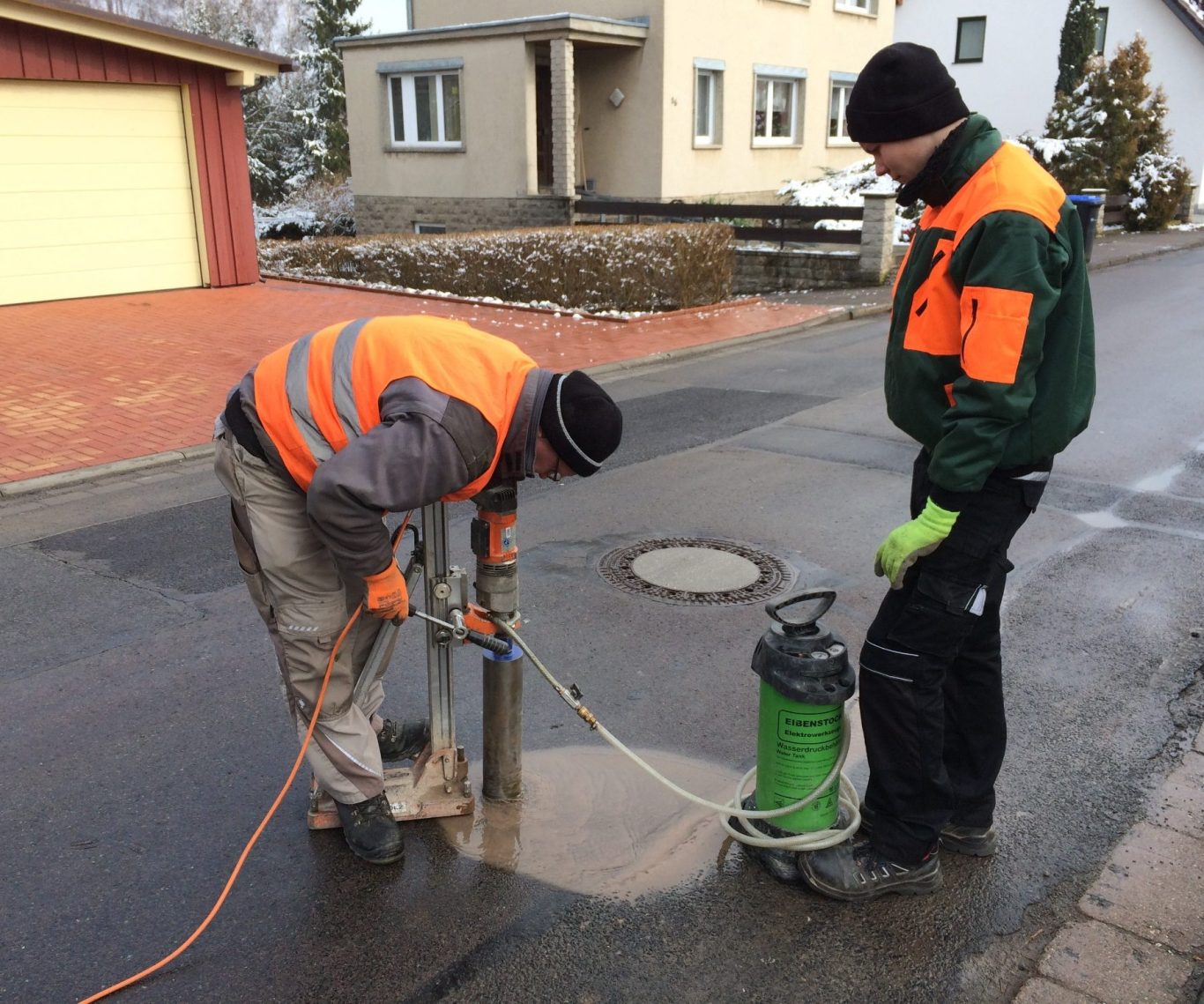 Probenentnahme im Asphalt: Zwei Arbeiter in Warnwesten untersuchen den Straßenbelag mit einer Maschine zur Boden- und Materialanalyse.
