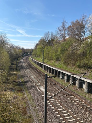 Eisenbahngleise, umgeben von Bäumen und grüner Landschaft, unter blauen Himmel.