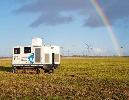 Drucksondiergerät (CPT) Raupe in einem Feld mit Windrädern im Hintergrund und einem Regenbogen am Himmel.